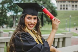 Selective Focus Portrait Photo of Smiling Woman in Black Academic Dress Holding Diploma Posing